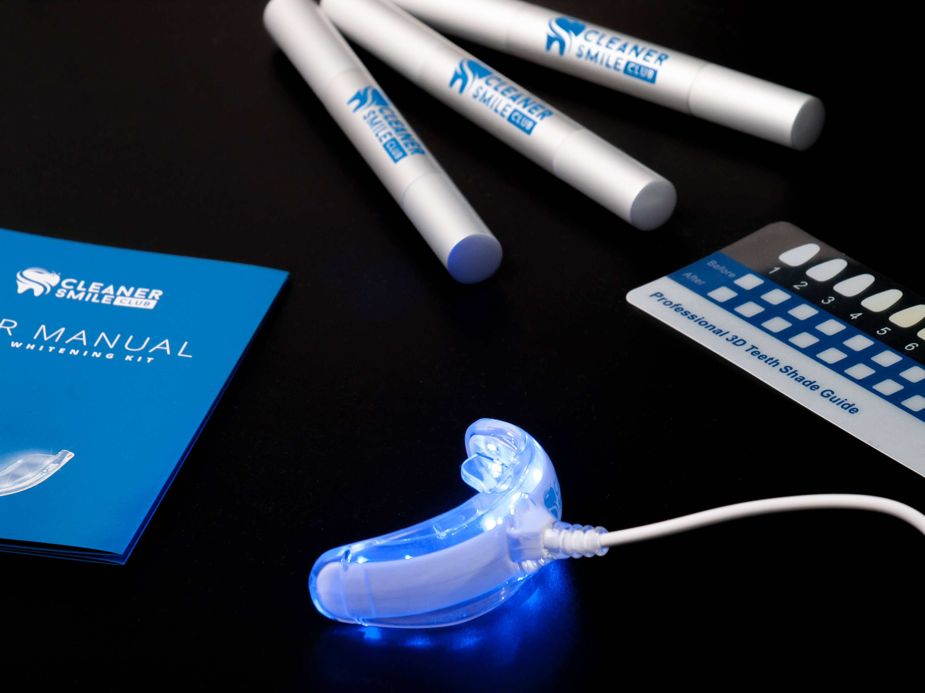 Effective teeth whitening kit from Cleaner Smile Club that consist from whitening pen, blue manual, stripe and LED mouth piece on the black background still photography production made by Fantastic Imago Branding, Advertising and Consulting Agency