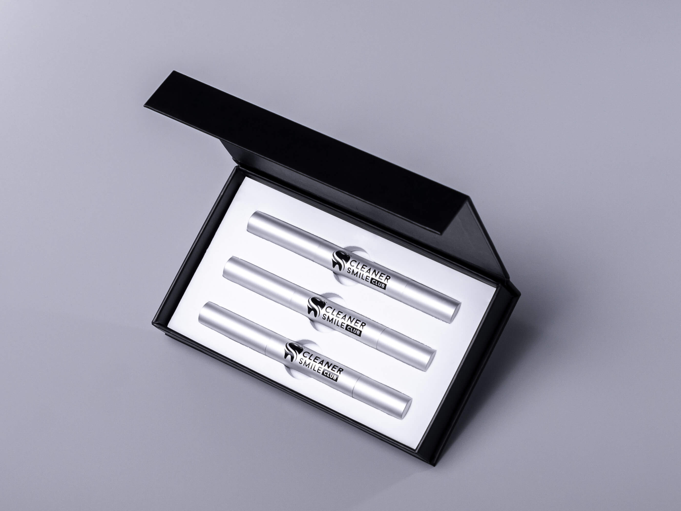 Very effective teeth whitening treatment black kit on the grey background with 3 whitening pens with black brand identity logo of the brand from Whitening Cosmetic Brand Cleaner Smile Club this pro photo production made by Fantastic Imago Branding, Advertising and Consulting Agency